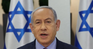 Benjamin Netanyahu falando, sério, com bandeiras de Israel ao fundo