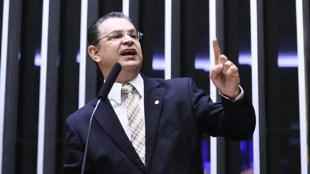 O líder do PL na Câmara dos Deputados, Sóstenes Cavalcante (PL-RJ), falando em microfone e apontando pra cima, sério, de óculos e roupa social, sem olhar para a câmera