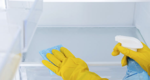 Pessoa com luvas amarelas limpando prateleiras de geladeira