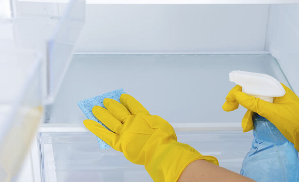 Pessoa com luvas amarelas limpando prateleiras de geladeira