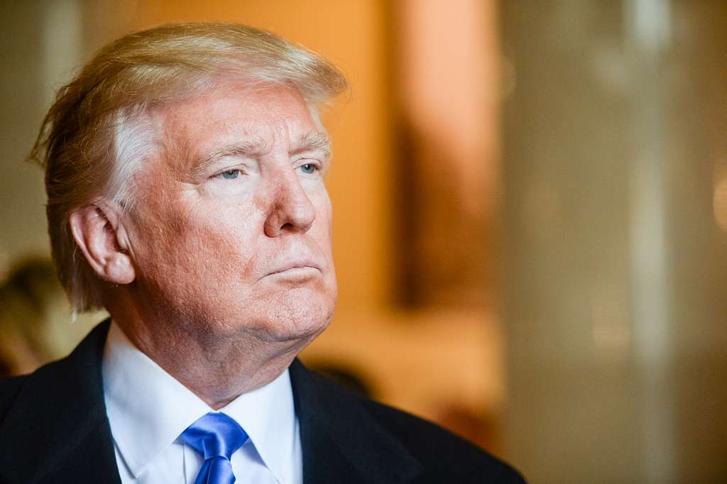 Donald Trump sério, no canto esquerdo de foto, de perfil