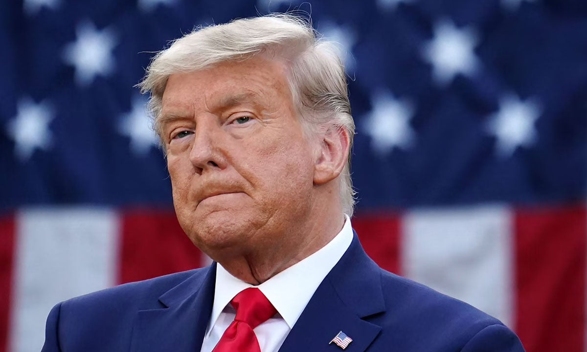 O presidente dos Estados Unidos, Donald Trump, com expressão pensativa e bandeira dos EUA ao fundo
