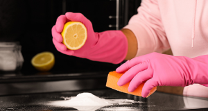 Pessoa com luvas de limpeza cor de rosa, segurando metade de um limão e bucha de limpeza