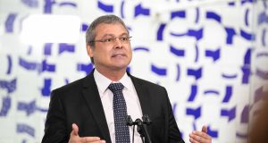 Lindbergh Farias falando e gesticulando, de óculos de grau e roupa social, sem olhar para a câmera