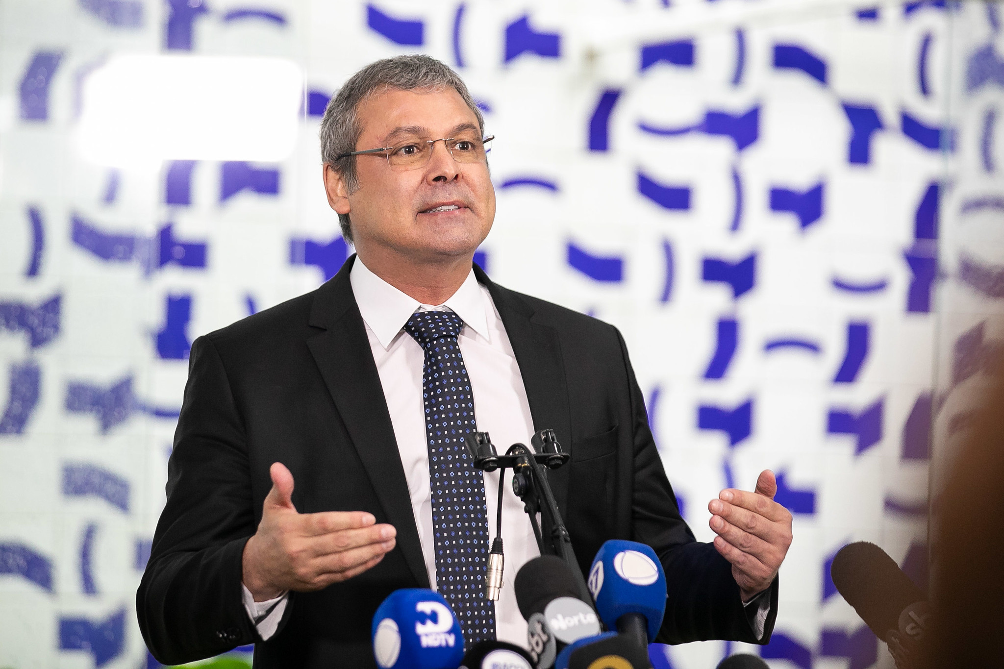 Lindbergh Farias falando e gesticulando, de óculos de grau e roupa social, sem olhar para a câmera