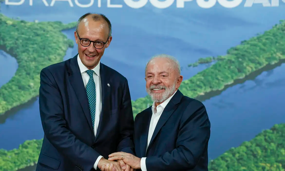 O primeiro-ministro da Alemanha, Friedrich Merz, e o presidente do Brasil, Lula, sorrindo em aperto de mãos