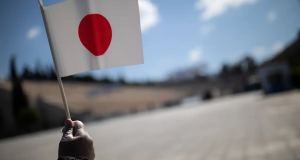 Mão com luva segurando pequena bandeira do Japão ao ar livre em dia ensolarado
