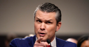 ecretário de Defesa, Pete Hegseth, olhando pra frente e apontando, sério