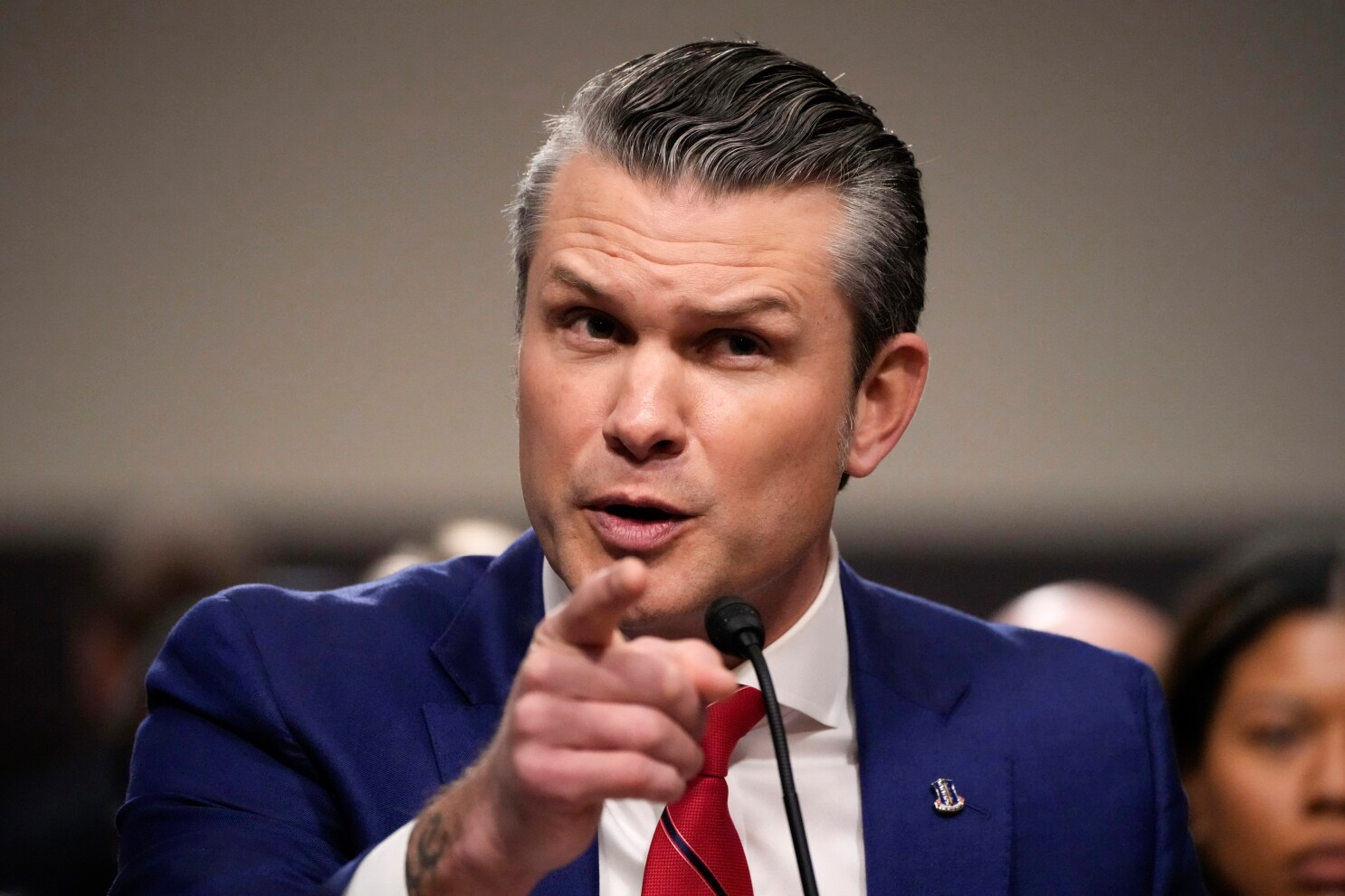 ecretário de Defesa, Pete Hegseth, olhando pra frente e apontando, sério