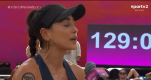 Carol Solberg falando em microfone, de viseira, de olhos fechados, de perfil