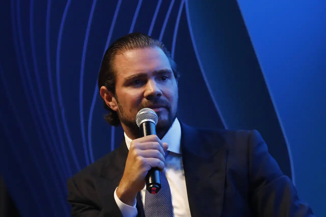 O presidente do Banco Master, Daniel Vorcaro, falando em microfone sem olhar para a câmera, sério