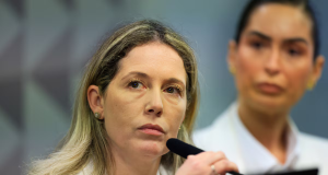 Thaísa Hoffmann Jonasson, mulher do ex-procurador-geral do INSS Virgílio de Oliveira Filho, séria, segurando microfone, de cabelo solto