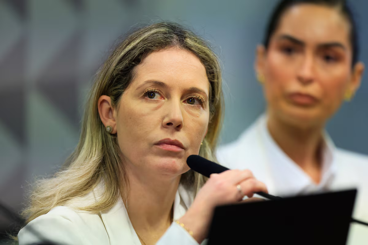 Thaísa Hoffmann Jonasson, mulher do ex-procurador-geral do INSS Virgílio de Oliveira Filho, séria, segurando microfone, de cabelo solto