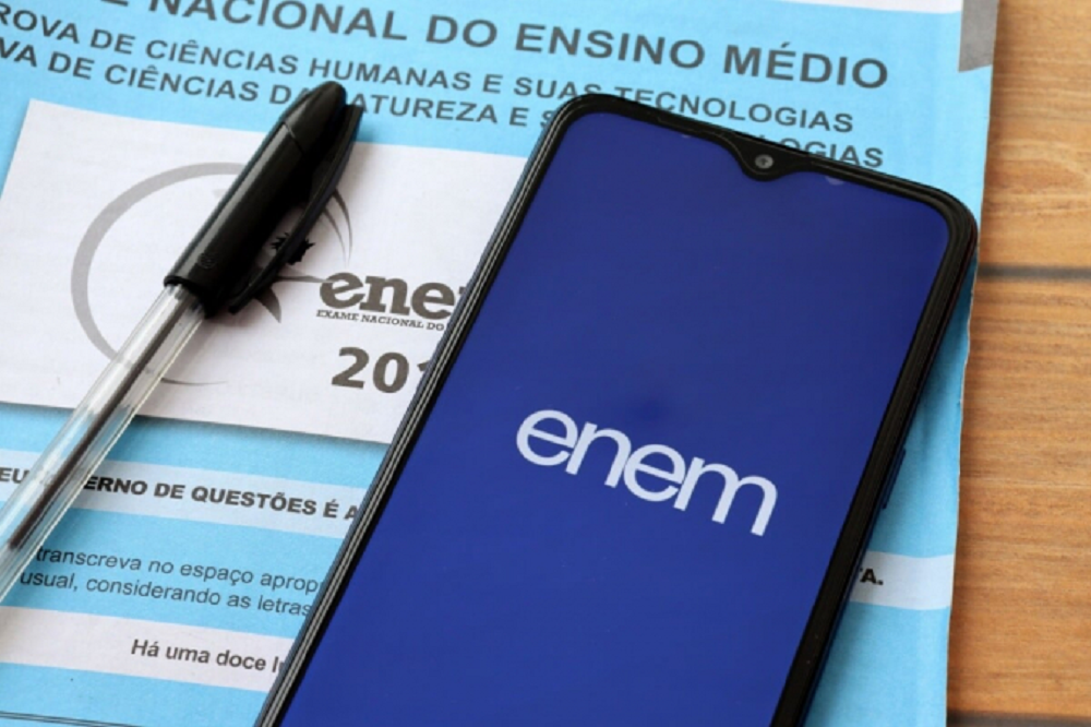 Caderno de questões do ENEM, caneta e celular com logo do ENEM