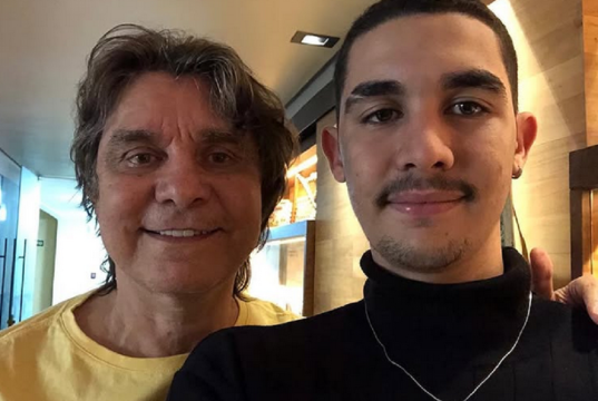 Lô Borges ao lado do filho Luca Arroyo Borges, posando para foto e sorrindo