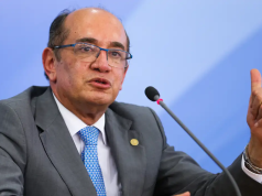 O ministro Gilmar Mendes, do STF (Supremo Tribunal Federal), falando e apontando pra trás, sério, de óculos
