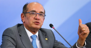 O ministro Gilmar Mendes, do STF (Supremo Tribunal Federal), falando e apontando pra trás, sério, de óculos
