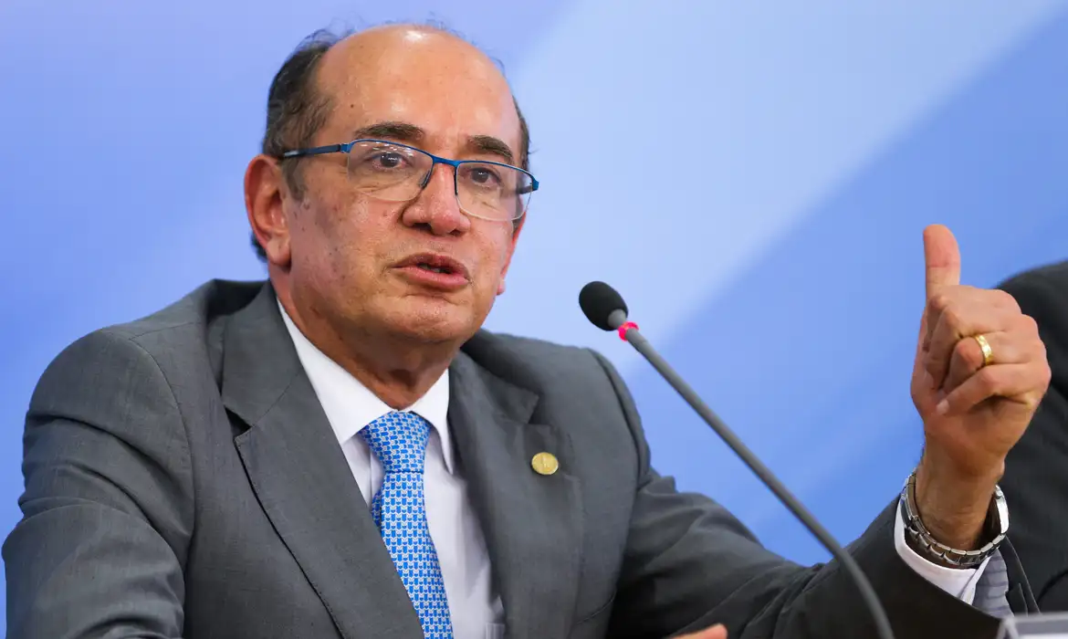 O ministro Gilmar Mendes, do STF (Supremo Tribunal Federal), falando e apontando pra trás, sério, de óculos