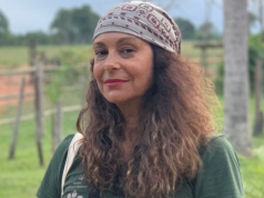 A atriz Giovanna Goldfarb de bandana e cabelo solto, maquiada, olhando séria para a câmera, ao ar livre