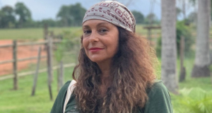 A atriz Giovanna Goldfarb de bandana e cabelo solto, maquiada, olhando séria para a câmera, ao ar livre