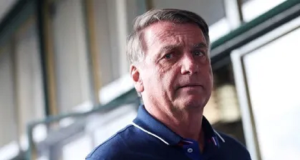 Jair Bolsonaro (PL) sério, sem olhar para a câmera, de camisa polo azul