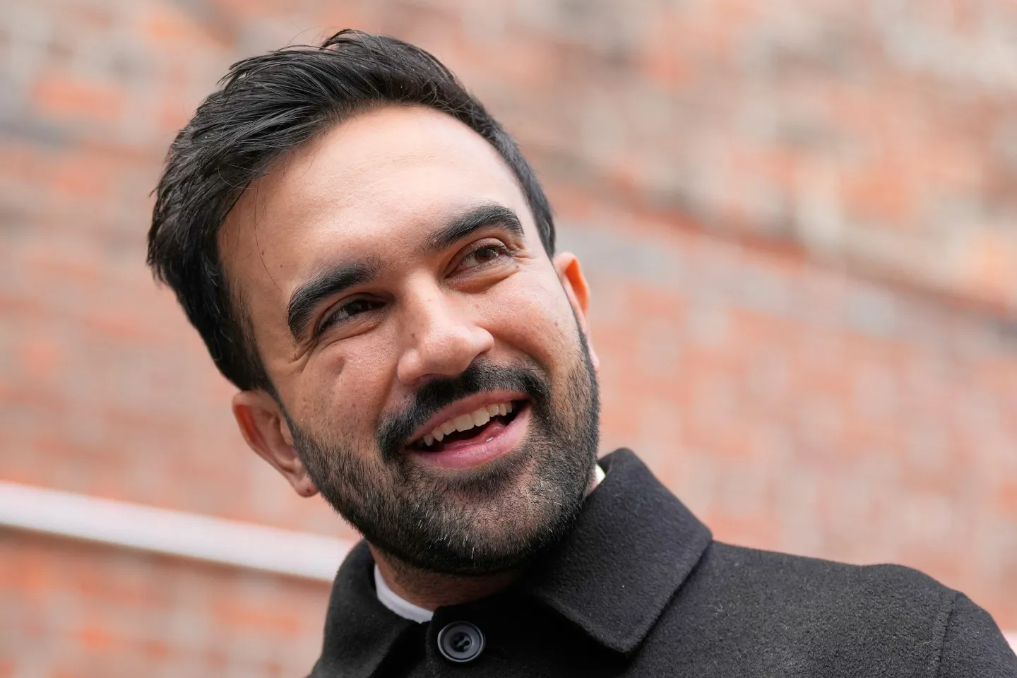 progressista Zohran Mamdani sorrindo sem olhar para a câmera