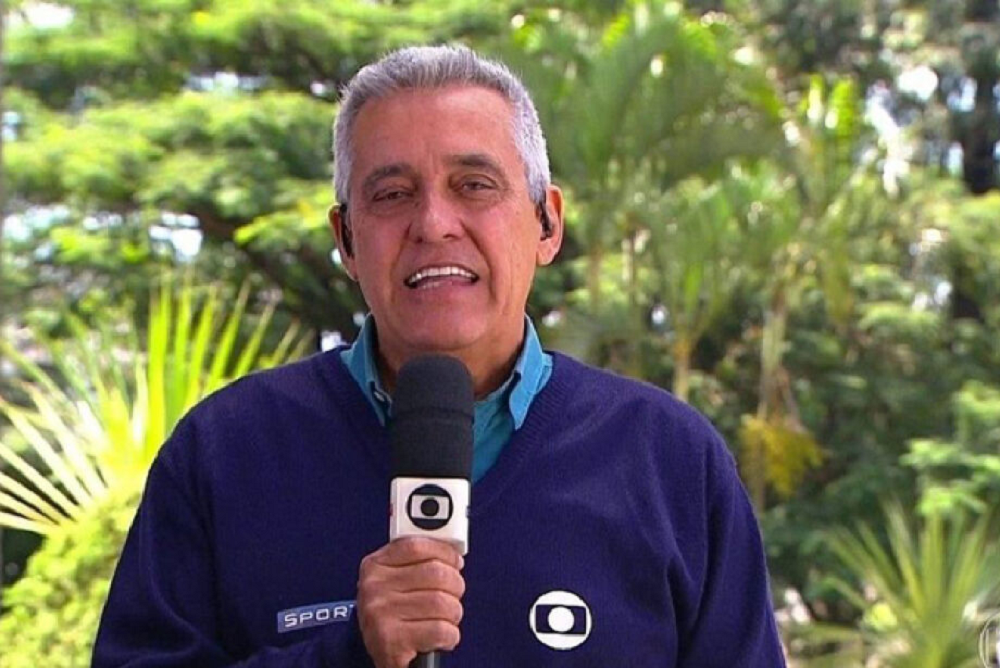 Mauro Naves com uniforme da Globo e microfone, falando para a câmera