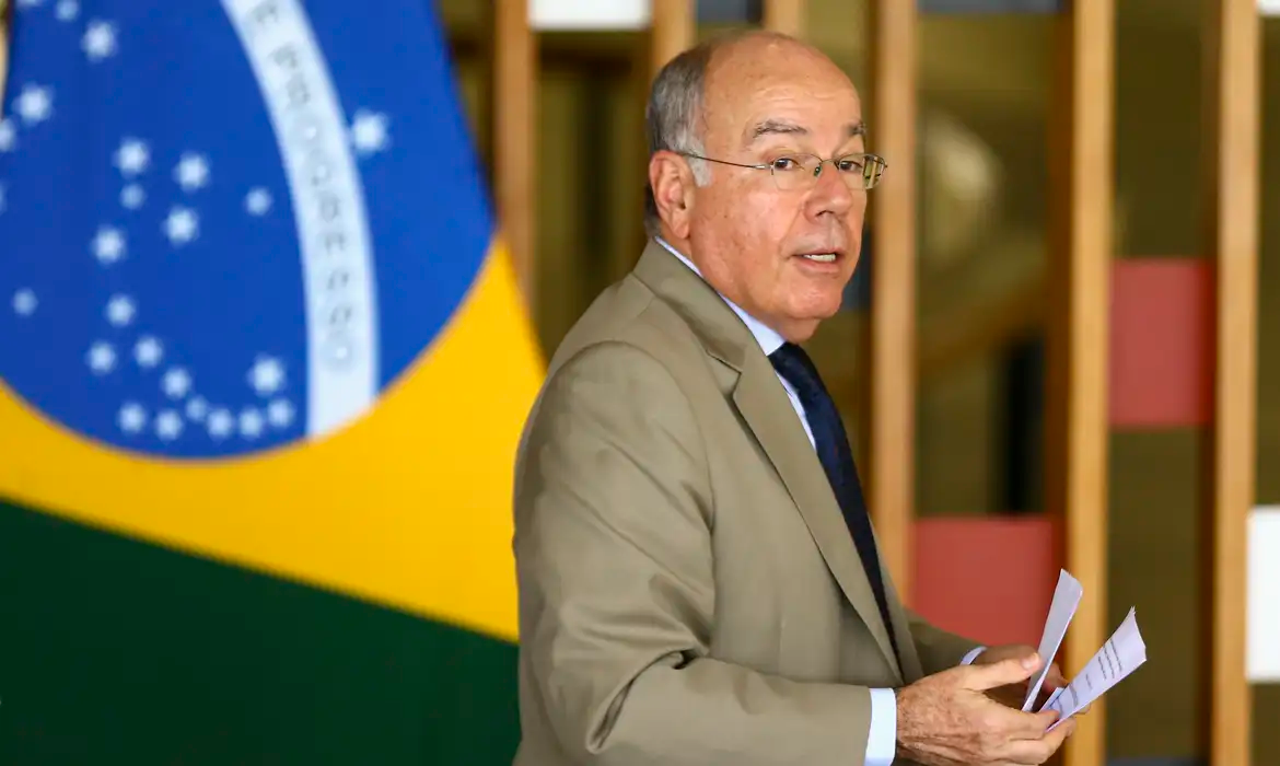 ministro das Relações Exteriores, Mauro Vieira, sério, com bandeira do Brasil ao fundo