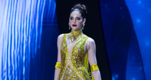 Fátima Bosch, recém-coroada Miss Universo, séria, de vestido dourado e amarelo, de cabelo preso, caminhando sem olhar para a câmera