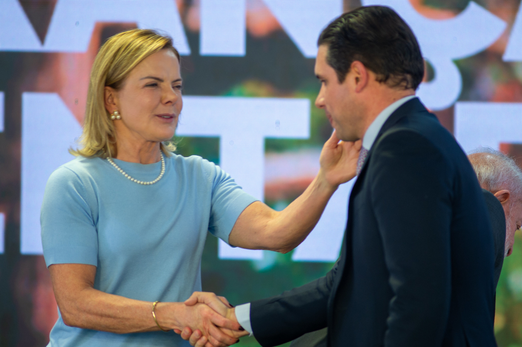 A ministra das Relações Institucionais, Gleisi Hoffmann, e o presidente da Câmara, Hugo Motta (Republicanos-PB), prestes a se abraçarem, e em aperto de mãos, em pé