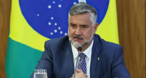 Paulo Pimenta sério, com bandeira do Brasil ao fundo
