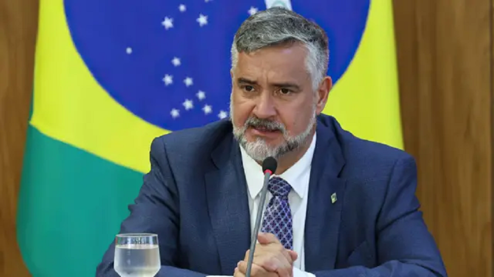 Paulo Pimenta sério, com bandeira do Brasil ao fundo