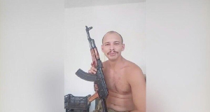 Philippe Marques Pinto no meio de montagem, sem camisa, segurando fuzil