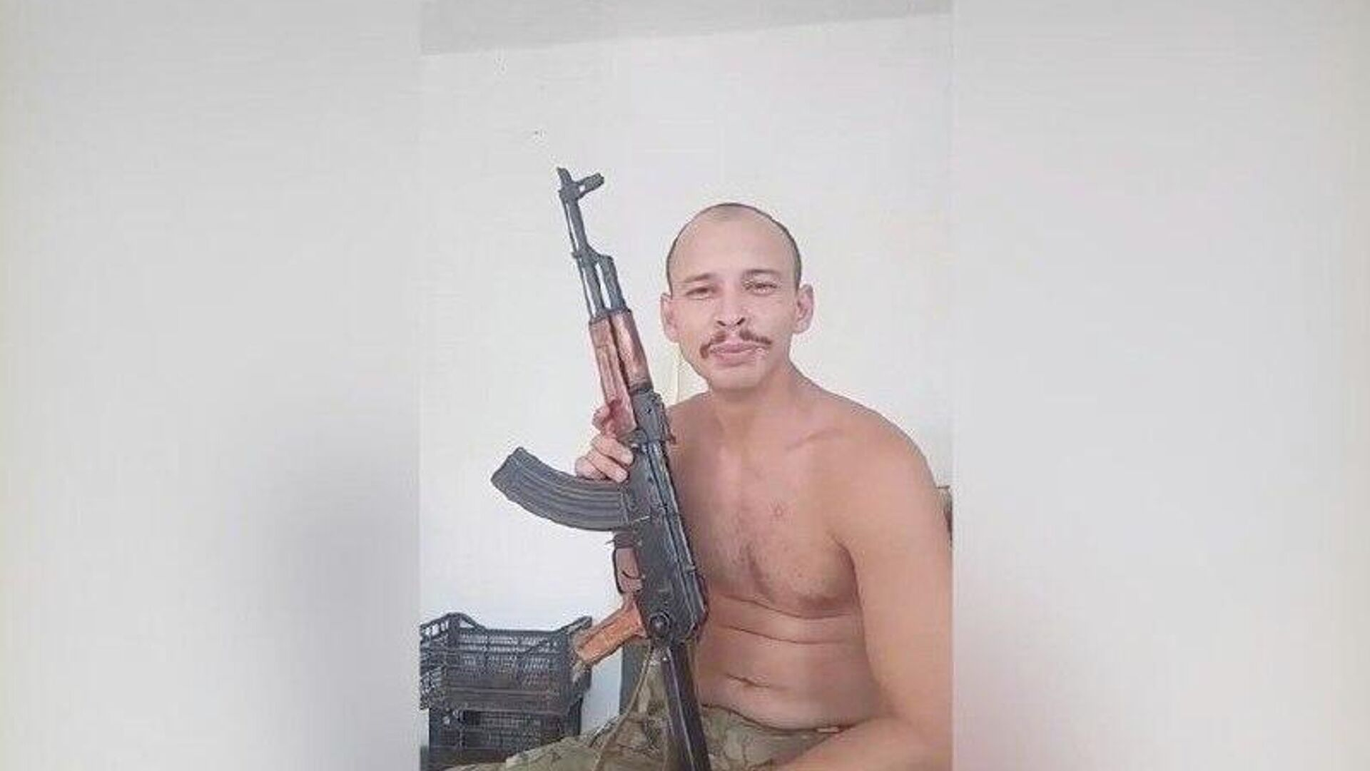 Philippe Marques Pinto no meio de montagem, sem camisa, segurando fuzil