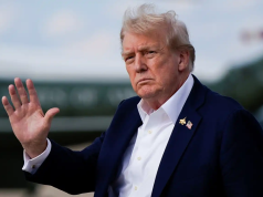 O presidente americano Donald Trump sério, sem olhar para a câmera, acenando ao ar livre