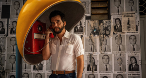 Wagner Moura em foto de divulgação de 'O Agente Secreto', no orelhão, em pé, sério