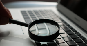 Mão segurando lupa perto de teclado de notebook