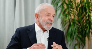 presidente Lula (PT) falando e gesticulando, sério, sem olhar para a câmera, sentado perto de mesa cheia de papéis