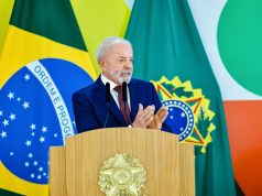 Lula (PT) em pé, falando em microfone e gesticulando, sério, olhando para o lado