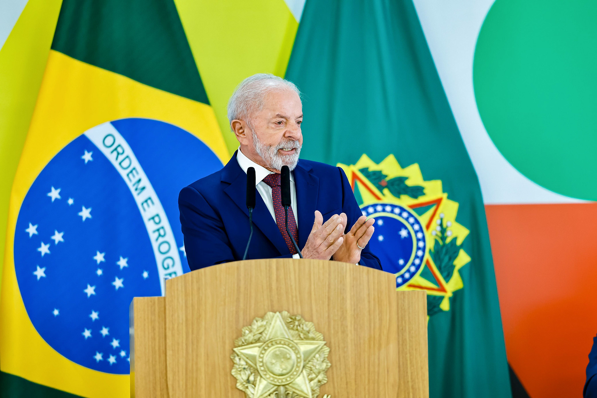 Lula (PT) em pé, falando em microfone e gesticulando, sério, olhando para o lado