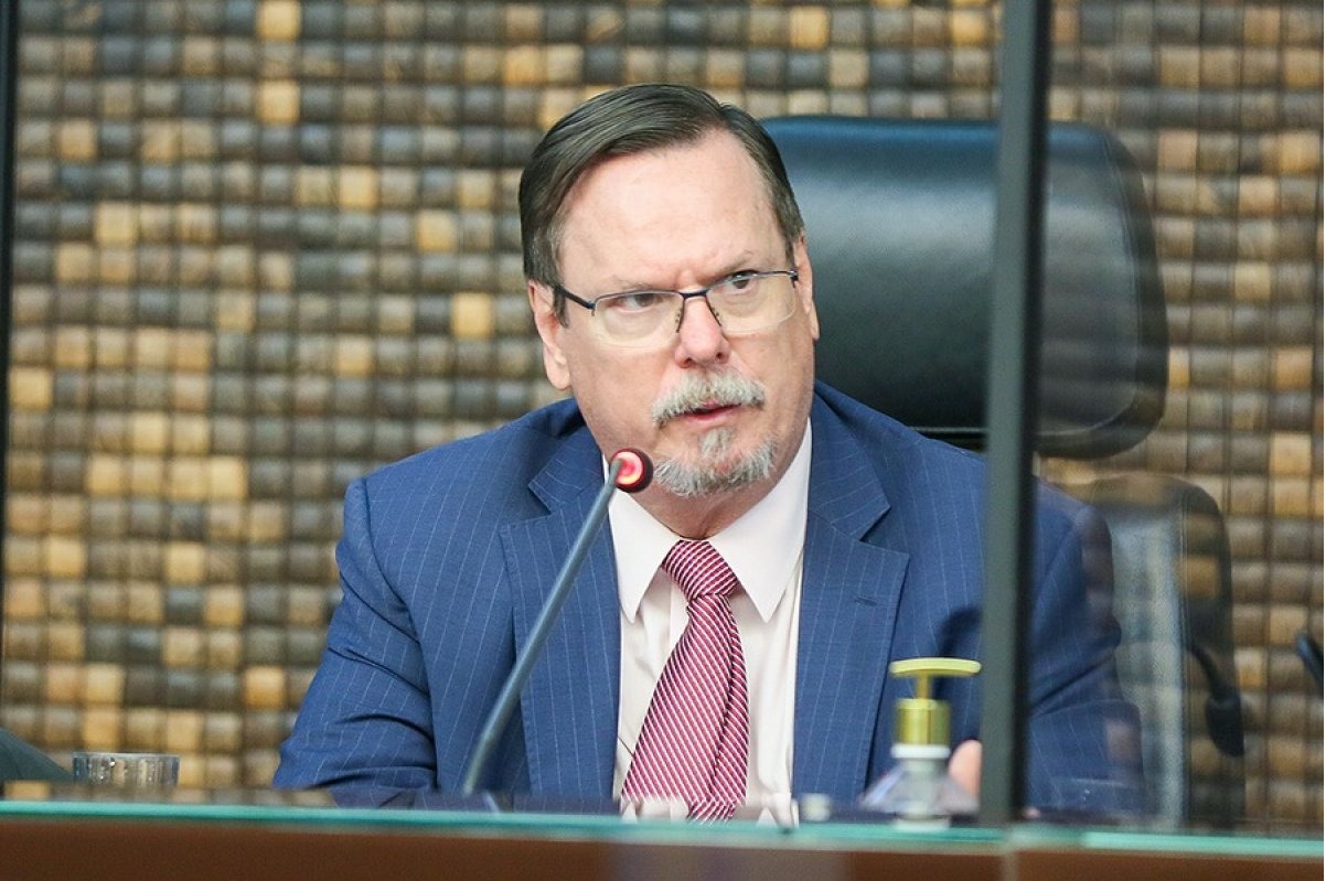 Carlos Vieira Von Adamek, auxiliar do ministro do STF Dias Toffoli, de óculos de grau e roupa social, falando em microfone, sério, sem olhar para a câmera