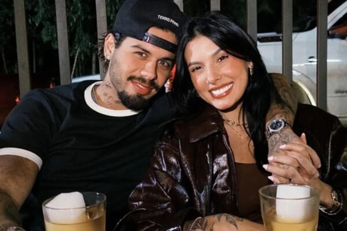 Zé Felipe e Ana Castela sentados lado a lado, sorrindo para a câmera, abraçados