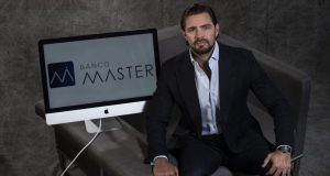 Daniel Vorcaro, dono do Banco Master, sentado ao lado de computador com a logo do banco, olhando para a câmera, sério