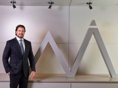 O dono do Banco Master, Daniel Vorcaro, em pé, sorrindo, perto de símbolo do banco