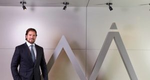 O dono do Banco Master, Daniel Vorcaro, em pé, sorrindo, perto de símbolo do banco