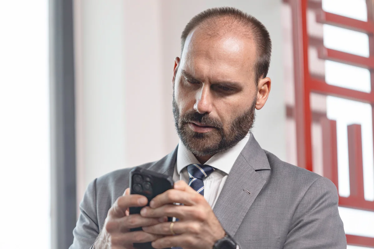 Eduardo Bolsonaro (PL-SP) mexendo no celular, de cabeça baixa, sério