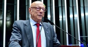 O senador Esperidião Amin (PP-SC) falando em microfone, sério, em pé, sem olhar para a câmera