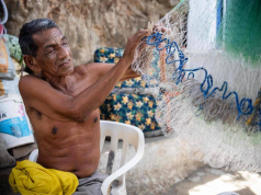 Alejandro Carranza, pai do pescador colombiano de mesmo nome que morreu, de bermuda cinza, sem camisa, segurando rede de pesca