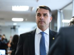 senador Flávio Bolsonaro (PL-RJ) sério, em pé, olhando levemente para o lado esquerdo da foto