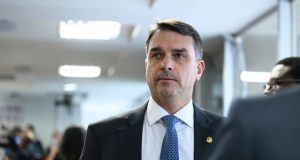 senador Flávio Bolsonaro (PL-RJ) sério, em pé, olhando levemente para o lado esquerdo da foto